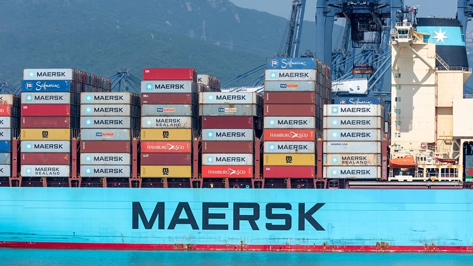 Maersk container ship stacked with shipping containers docked at a port with gantry cranes