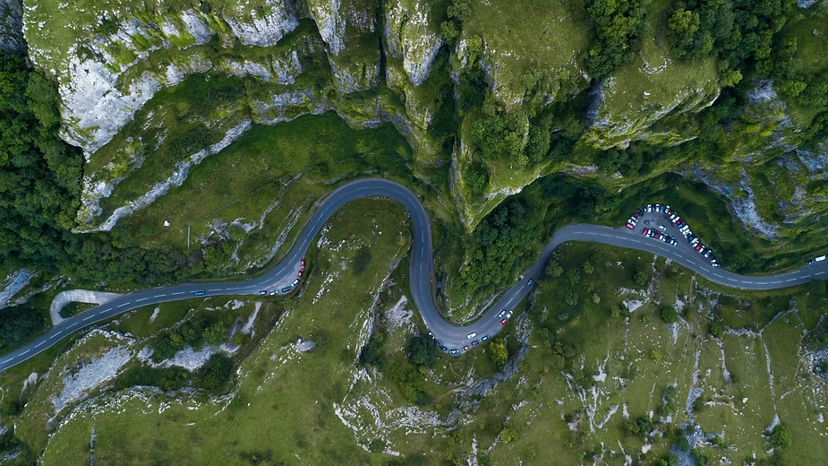 Aerial drone photo of a winding mountain road cutting through green cliffs, with cars parked along its bends